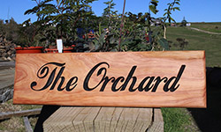 macrocarpa sign 500 x 140 "the orchard" with plants in the background